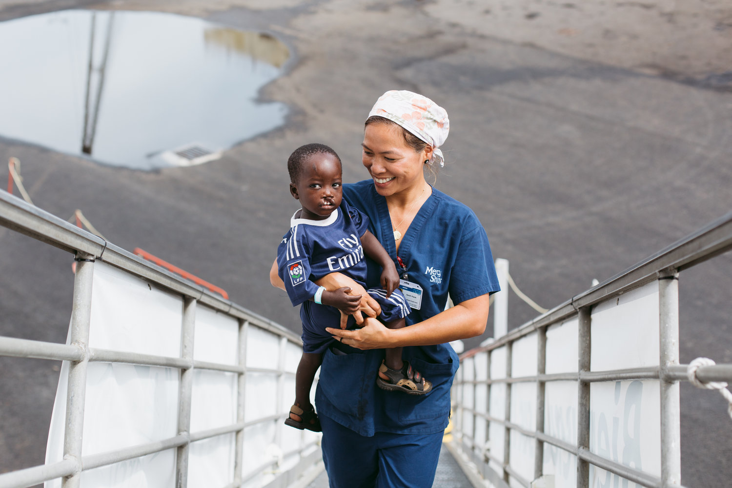 Sarah Kwok, Anesthesia Supervisor, carries cleft lip patient, Saliou up the ship's gangway for needed medical treatment.